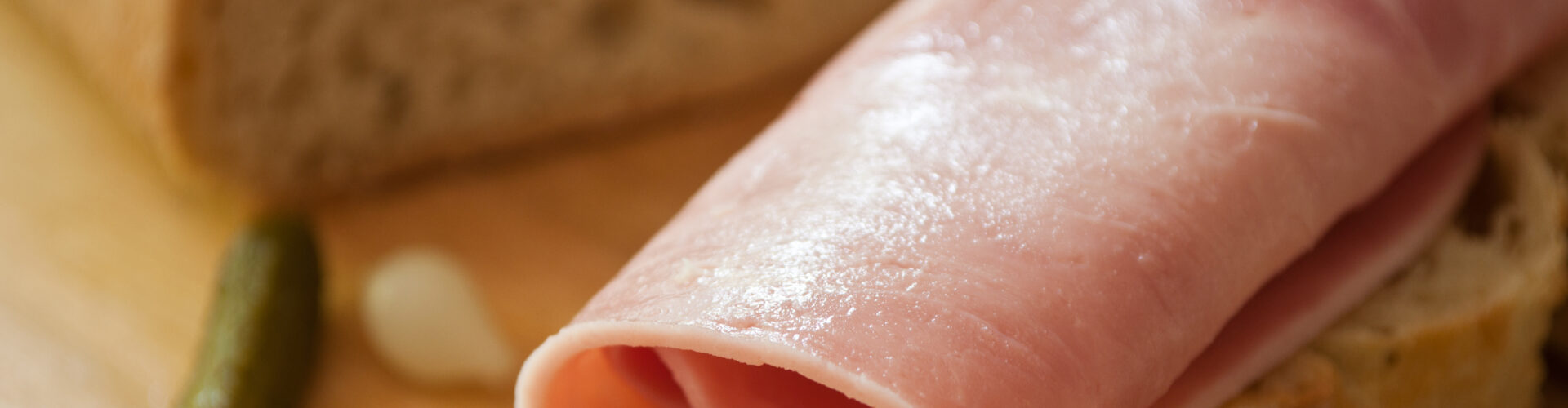 sliced ham on country bread with decorative gherkin and onion on wooden cutting board