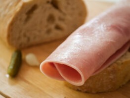 sliced ham on country bread with decorative gherkin and onion on wooden cutting board