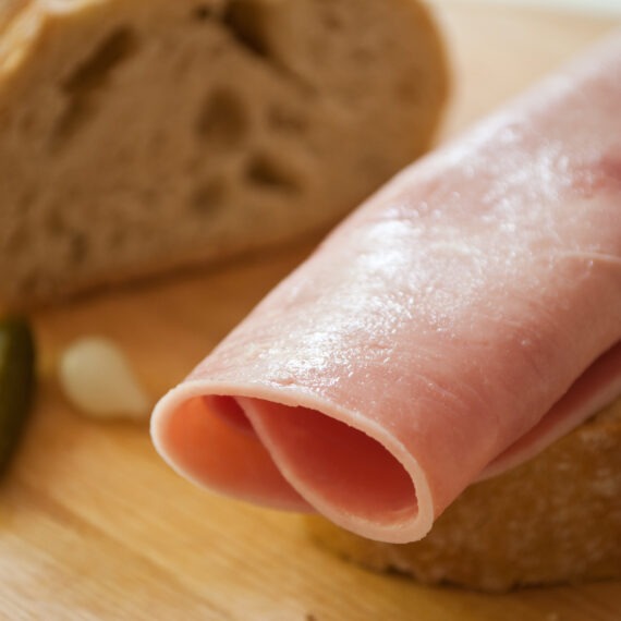 sliced ham on country bread with decorative gherkin and onion on wooden cutting board